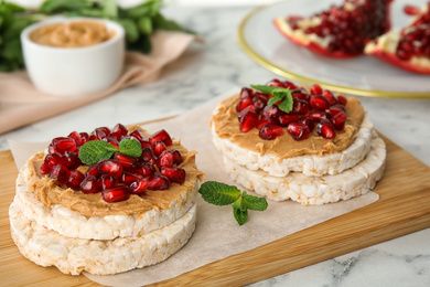 Puffed rice cakes with peanut butter, pomegranate seeds and mint on table, closeup