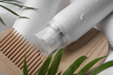 Wet bottle of dry shampoo spray and wooden comb on white towel, closeup