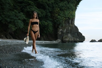 Beautiful young woman in stylish bikini on seashore, space for text