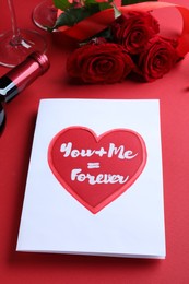 Photo of Card with romantic message, wine and roses on red background, closeup. Love confession
