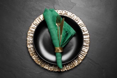 Plate with green fabric napkin, decorative ring and cutlery on black table, top view