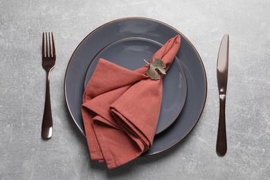 Plates with fabric napkin, decorative ring and cutlery on gray background, flat lay