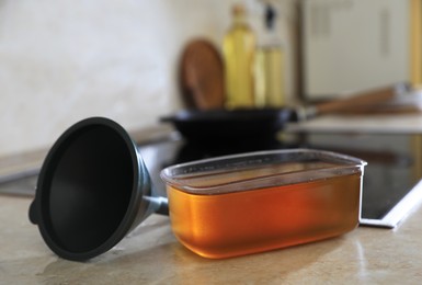 Photo of Container with used cooking oil and funnel near stove on kitchen counter