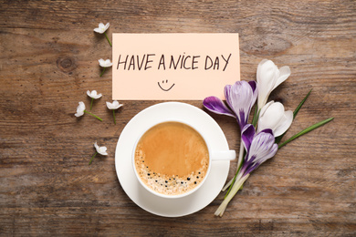 Morning coffee, flowers and card with HAVE A NICE DAY wish on wooden table, flat lay
