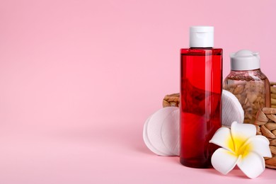 Bottles of micellar water, plumeria flower and cotton pads on pink background. Space for text