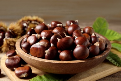 Photo of Fresh sweet edible chestnuts on wooden board, closeup