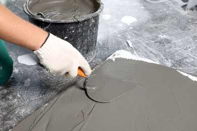 Worker spreading wet concrete with trowel indoors, closeup