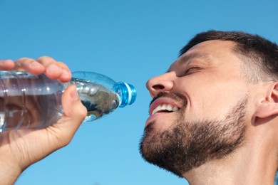 Photo of Happy man drinking water against blue sky on hot summer day, closeup. Refreshing drink