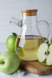 Jug of tasty juice and fresh ripe green apples on white wooden table, closeup