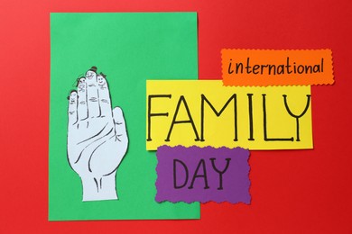 Paper cards with text International Family Day and hand cutout on red background, flat lay