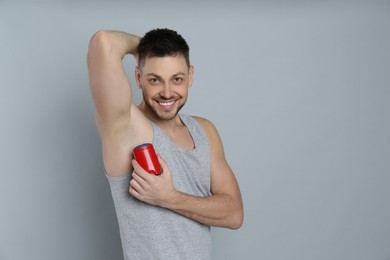 Handsome man applying deodorant on grey background. Space for text