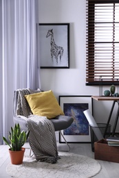 Comfortable armchair and table near window with horizontal blinds