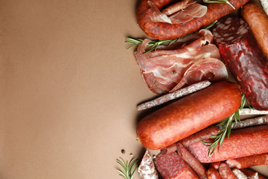 Different types of sausages with rosemary on brown background, flat lay. Space for text
