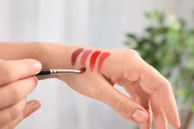 Woman testing and choosing lip gloss color on hand, closeup