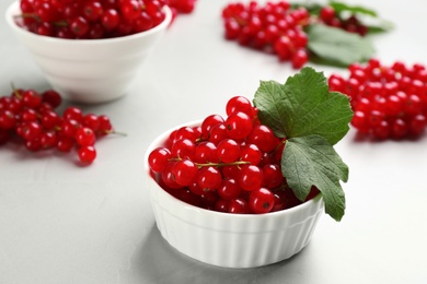Delicious red currants and leaves in bowl on light table