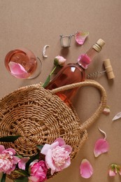 Flat lay composition with rose wine, wicker bag and beautiful pink peonies on brown background