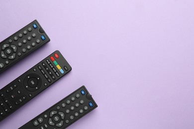 Remote controls on violet background, flat lay. Space for text