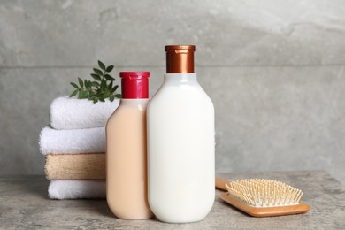 Photo of Bottles of shampoo, hairbrush and stacked towels on grey table