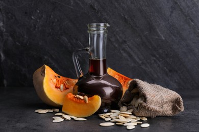Fresh pumpkin seed oil in glass jug on dark grey table