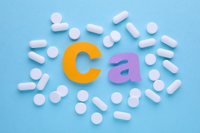 Calcium symbol made of colorful letters and white pills on light blue background, flat lay