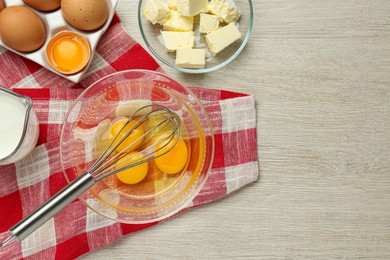 Whisk, eggs in bowl, milk and butter on white wooden table, flat lay. Space for text