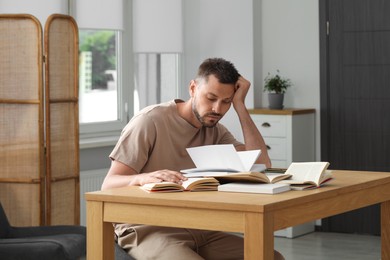 Sleepy man studying at wooden table indoors