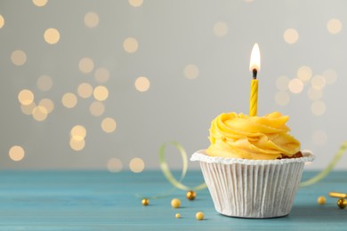 Tasty birthday cupcake on light blue wooden table against blurred lights. Space for text