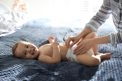 Photo of Mother changing baby's diaper on bed at home
