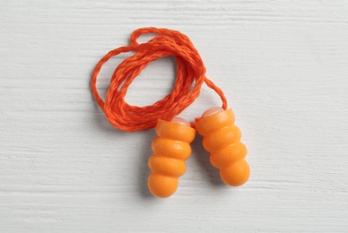 Pair of orange ear plugs with cord on white wooden background, top view