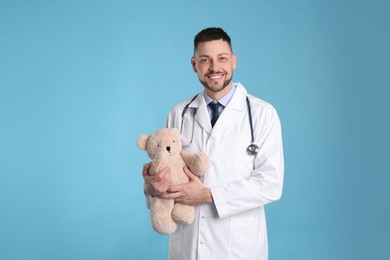 Photo of Pediatrician with teddy bear and stethoscope on light blue background
