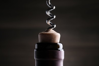 Opening wine bottle with corkscrew on dark background, closeup