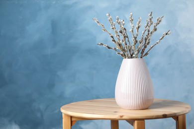 Beautiful bouquet of pussy willow branches in vase on wooden table. Space for text