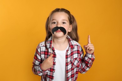 Photo of Funny little girl with fake mustache on yellow background