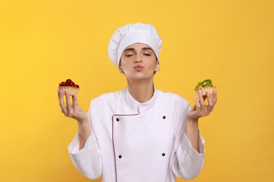 Photo of Professional confectioner in uniform with delicious tartlets on yellow background