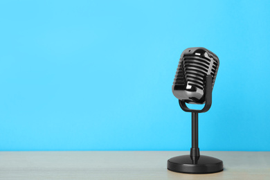 Retro microphone on wooden table against light blue background, space for text. Interview