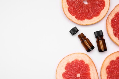 Bottles of citrus essential oil and fresh grapefruit slices on white background, flat lay. Space for text