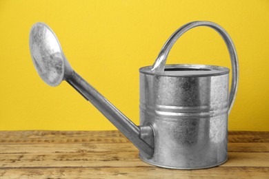 Photo of Metal watering can on wooden table against yellow background