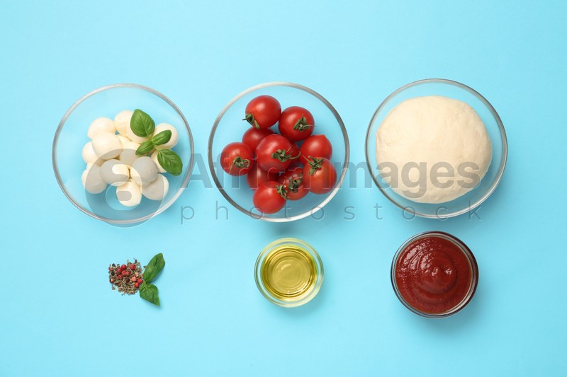 Photo of Raw dough and other ingredients for pizza on light blue background, flat lay