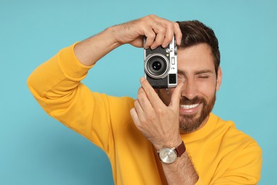 Man with camera taking photo on light blue background. Interesting hobby