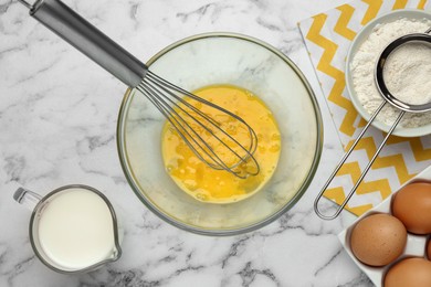 Whisked eggs and other ingredients on white marble table, flat lay