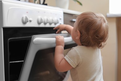 Photo of Little child opening oven indoors. Dangers in kitchen