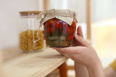 Woman putting jar of pickled vegetables on shelf indoors, closeup