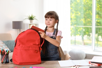 Schoolgirl putting stationery into backpack at home