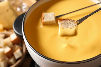 Dipping pieces of bread into tasty cheese fondue, closeup