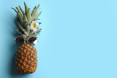 Photo of Top view of funny pineapple with sunglasses and plumeria flower on light blue background, space for text. Creative concept