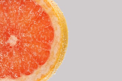 Slice of grapefruit in sparkling water on light background, closeup with space for text. Citrus soda