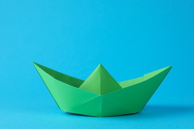 Handmade green paper boat on light blue background. Origami art