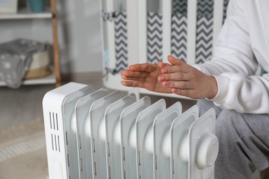 Photo of Young woman warming hands near modern electric heater indoors, closeup