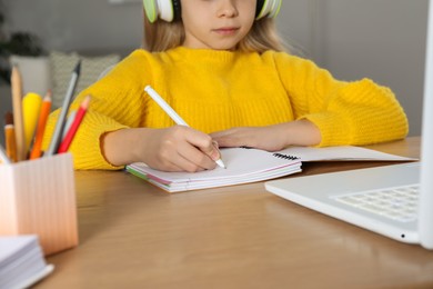 Photo of Cute little girl with modern laptop studying online at home, closeup. E-learning