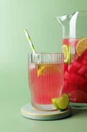 Tasty summer watermelon drink with lime in jug and glass on pale light green background. Space for text